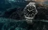 Unbranded black bezel dive watch at the boundary of water and volcanic stone
